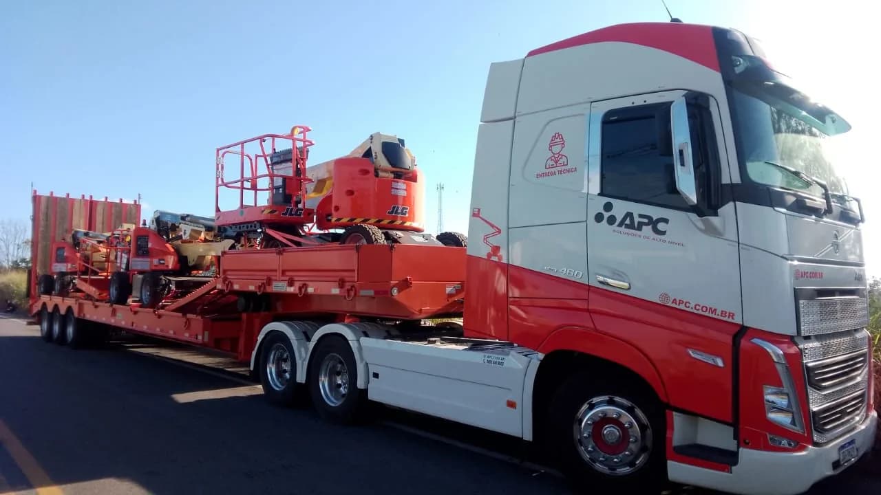 Carreta do Grupo APC na estrada, carregada com plataformas de lança JLG, com o logo da APC na porta do caminhão