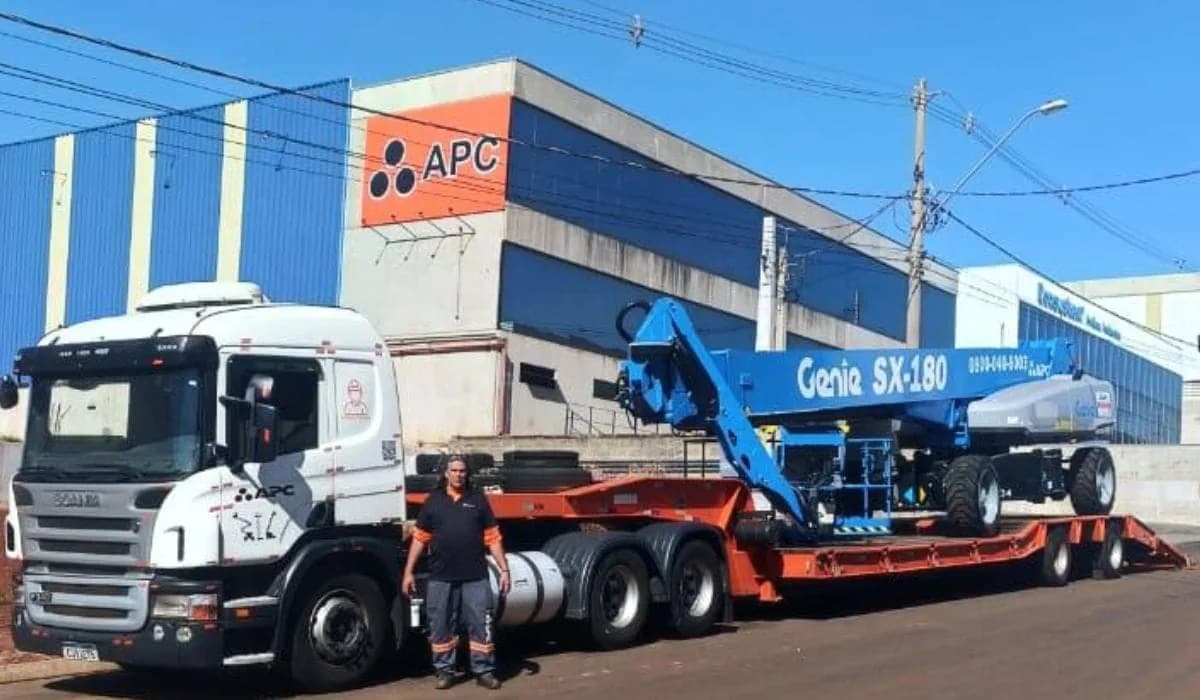 Caminhão do Grupo APC com uma plataforma Genie SX-180 carregada, em frente ao galpão da empresa