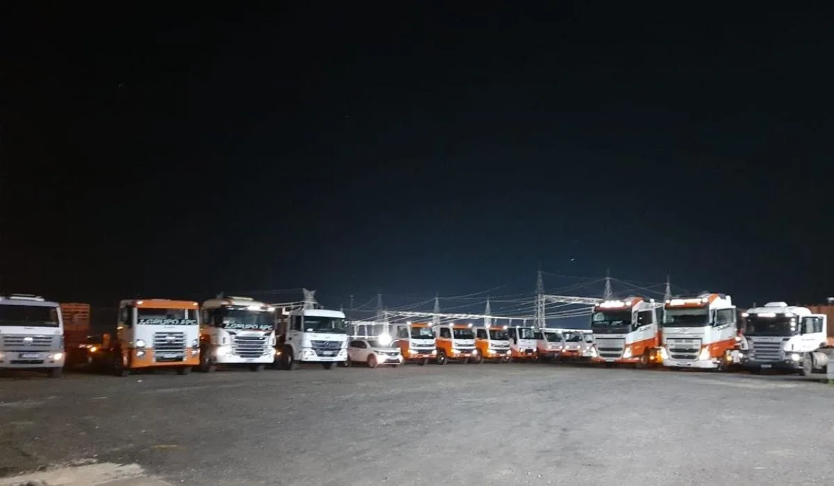 Caminhões do Grupo APC estacionados lado a lado na garagem da empresa, à noite